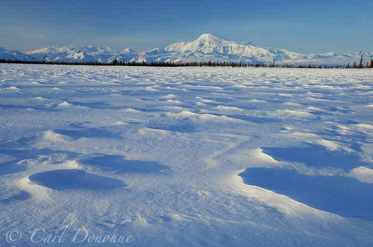 Photo of Mount Sanford, one of the highest peaks in the Wrangell Mountains, at dawn, from a small frozen kettle pond. Winter snow creates patterns on the frozen lake. Mt. Sanford, Wrangell - St. Elias National Park and Preserve, Alaska.