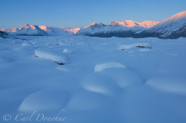 Snow-covered boulders of the Kennicott Glacier moraine. In the distance lie Bonanza Ridge, Regal Mountain and Donoho Peak, of the Wrangell Mountains. Wintertime at Kennicott, Wrangell-St. Elias National Park and Preserve, Alaska.