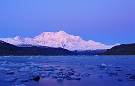 Mount Saint Elias glows in the soft after dusk alpenglow of the winter sky. Icy Bay in the foreground is littered with scattered icebergs, remnants from the many glaciers in the area. Mount Saint Elias and Icy Bay, Wrangell-St. Elias National Park and Preserve, Alaska.
